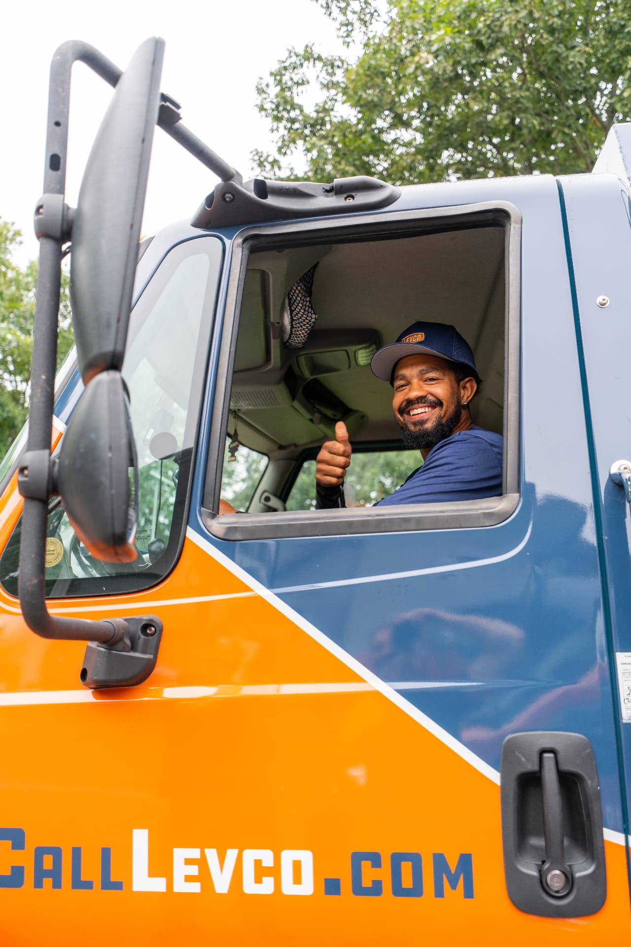 Smiling Levco delivery driver waving from the cab of a Levco truck