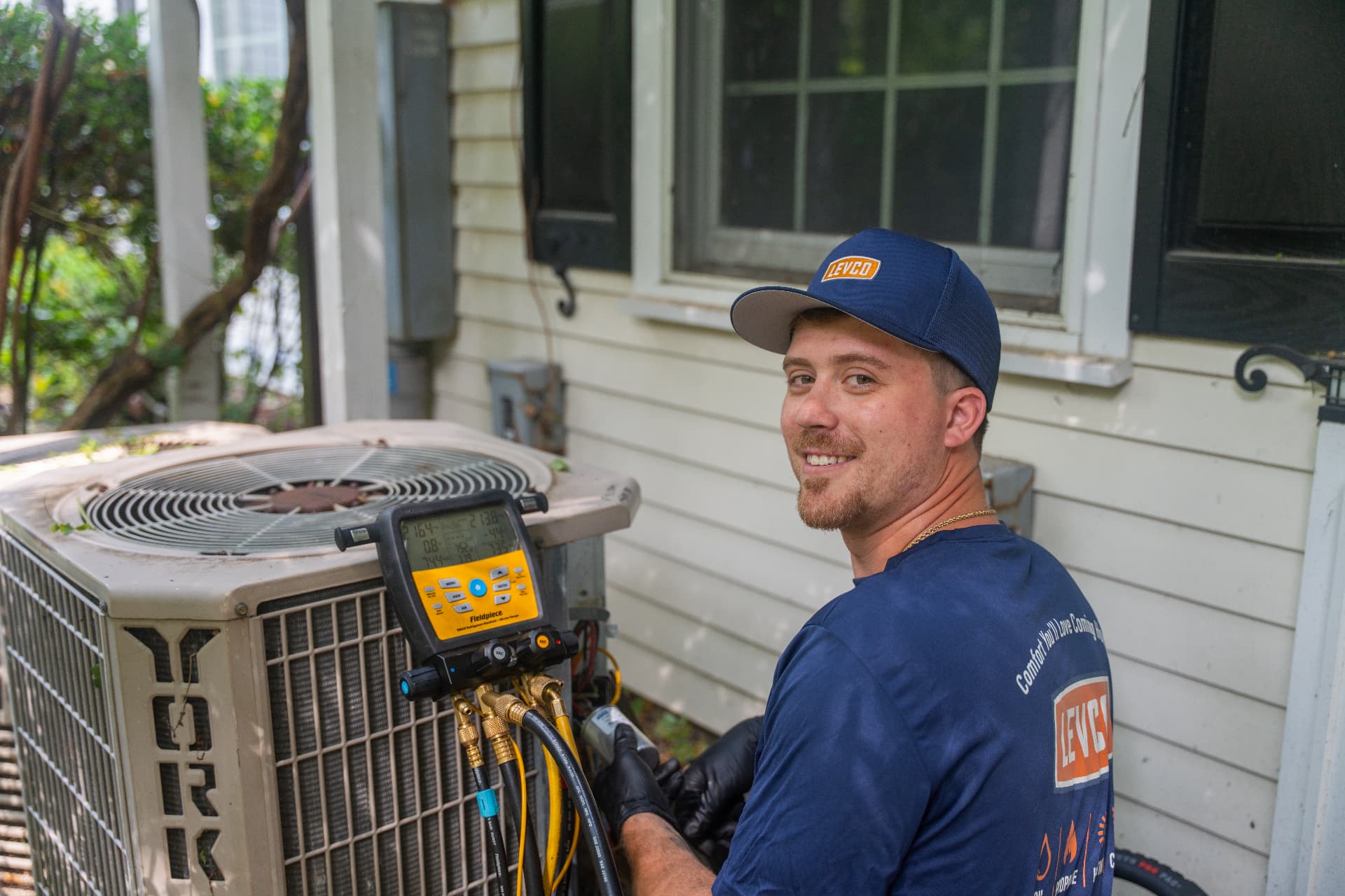 Levco technician inspecting a residential air conditioner with diagnostic gauges