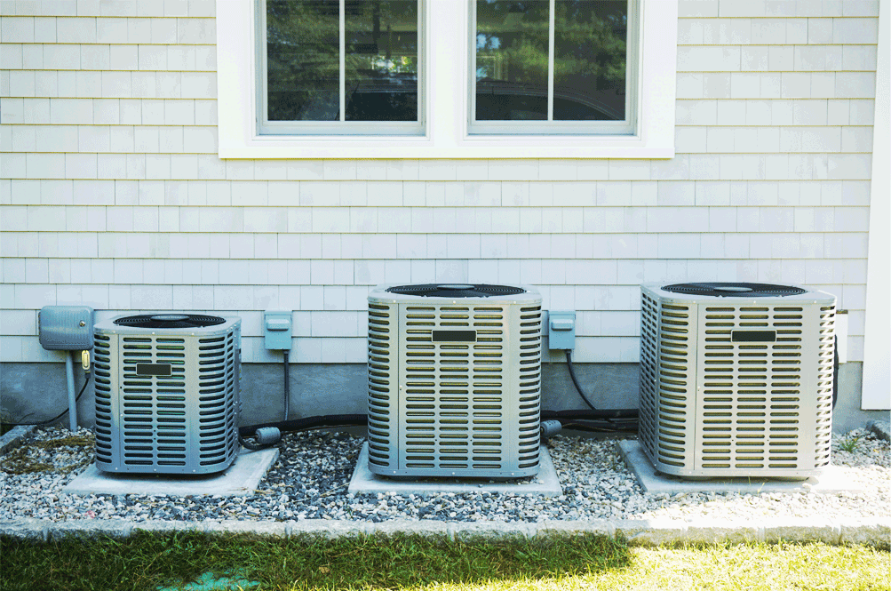 Three central air conditioning condenser units installed beside a Connecticut home