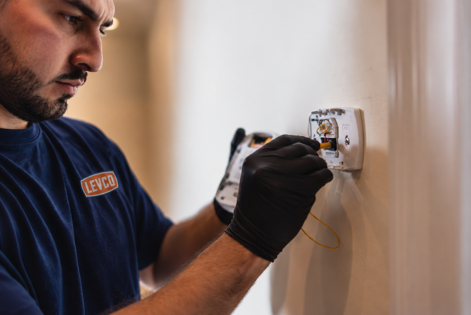 Levco technician checking the wiring behind a wall thermostat