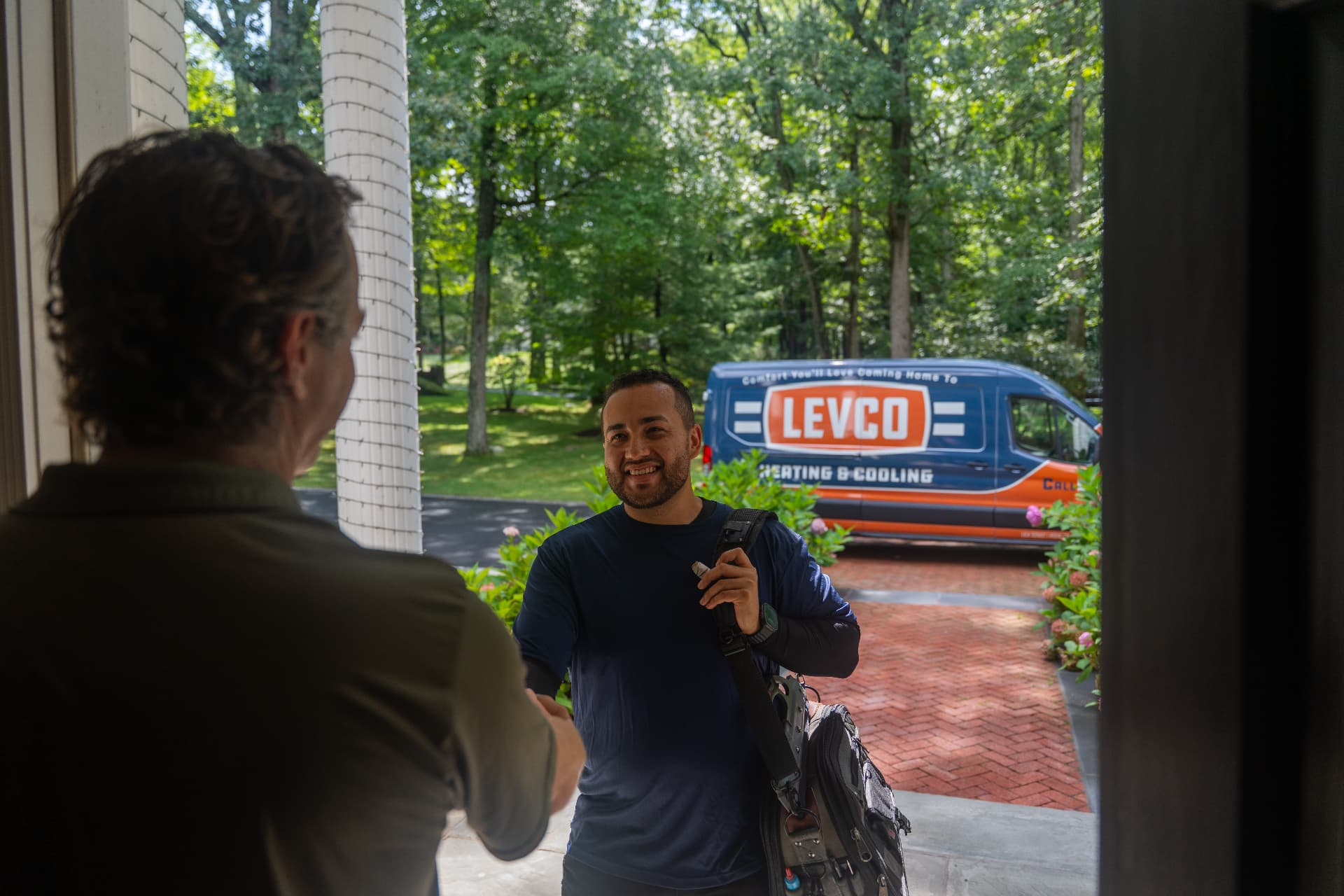 Levco technician greeting a homeowner at the front door with the service van in the driveway